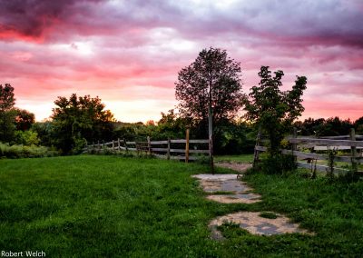 "vivid sunset over a horse pasture with stone path and wooden fence"