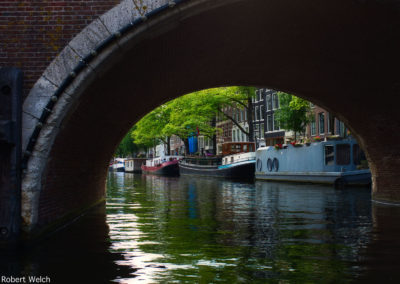 view of canal boats through an arched bridge in Amsterdam