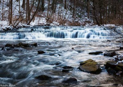 "icy stream with waterfall rocks and snow"