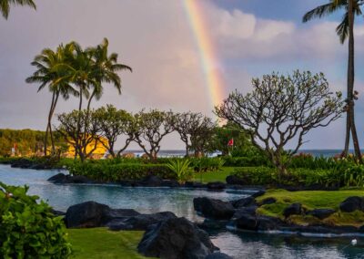 rainbow over Shipwreck beach in Kauai with palm trees rocks and garden