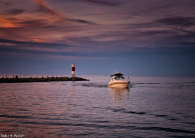 "motorboat passing a breakwall and channel marker on Lake Ontario at sunset"