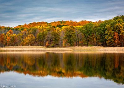 "brilliant fall scene with yellow orange and red trees reflected in a pond"