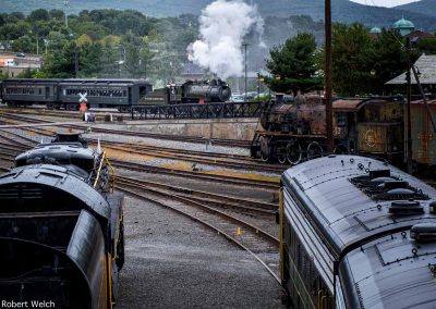 "Baldwin 0-4-0 pulls passenger cars as antique locomotives sit in yard"
