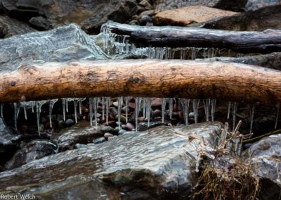 icicles beneath a driftwood log, with icy pebbles in Webster Park at Lake Ontario
