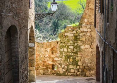 "ancient walled lane in montepulciano Italy with blue sky and trees on distant hills"